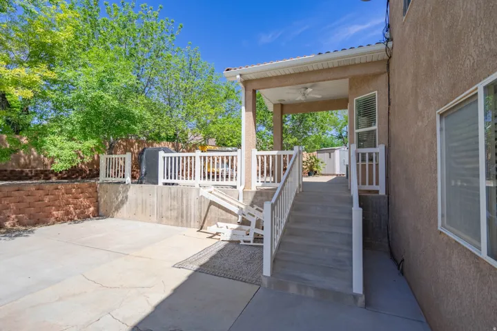 Covered patio with a ceiling fan, concrete stairs with white railings, and a concrete patio area