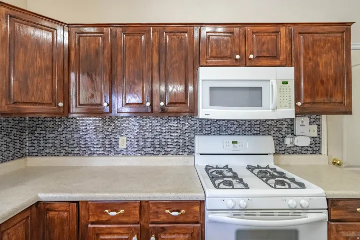 Kitchen featuring rich wood cabinetry, neutral countertops, a mosaic tile backsplash, and a white gas range with an overhead microwave