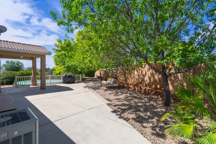 Expansive concrete patio with covered area, surrounded by mature trees and a privacy fence