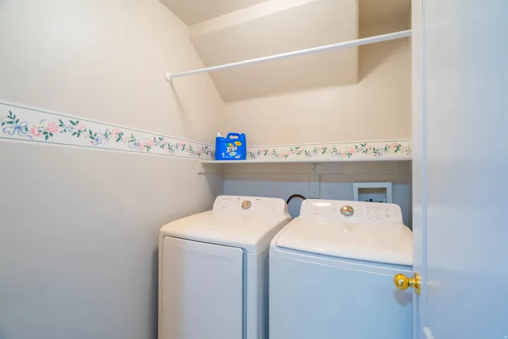 Dedicated laundry area with a built-in hanging rod, wall shelving, and a floral wallpaper border