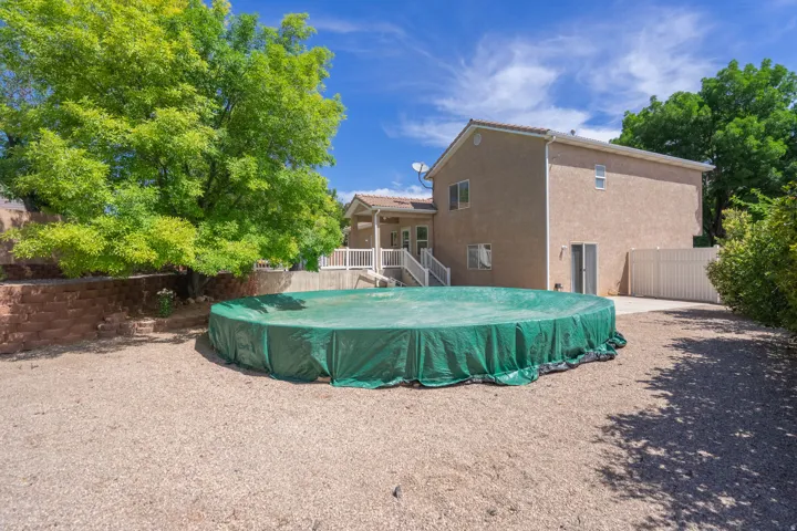 Spacious gravel yard featuring an above-ground pool, a terraced retaining wall, and mature trees