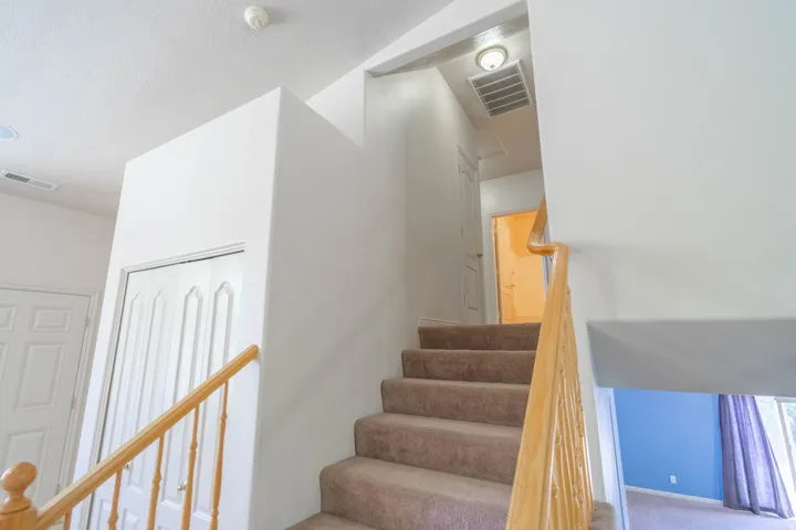 Carpeted staircase with light wood banister and spindles, leading to an upper hallway with a built-in light fixture and air vent