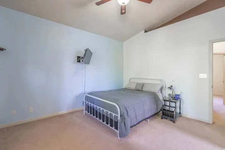 Carpeted room featuring a vaulted ceiling with exposed beams, and a ceiling fan with integrated lighting