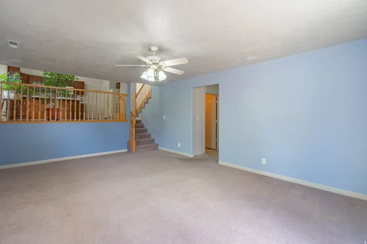 Carpeted living space featuring a ceiling fan, light blue walls, and white baseboards
