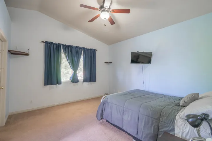 Interior room featuring a vaulted ceiling with a ceiling fan, light blue wall, and window with blinds