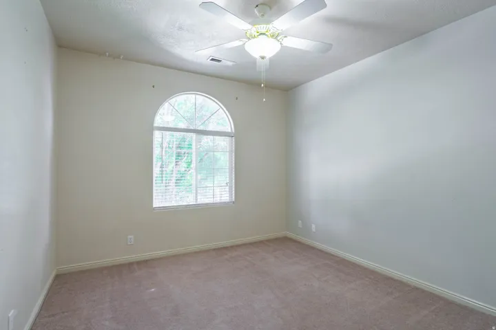 Spacious room with light-colored carpeting, an arched window, white window blinds, a ceiling fan with integrated lighting, and neutral wall tones
