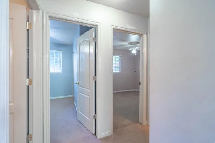 Hallway featuring two rooms with neutral-toned carpet flooring and white trim