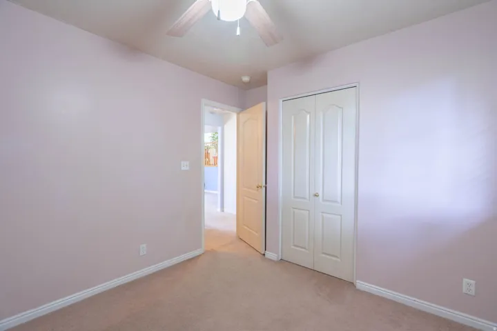 Carpeted room featuring a ceiling fan, light-colored walls, white baseboards, and a bi-fold closet door