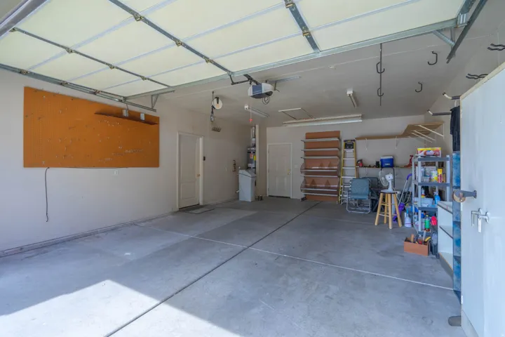 Spacious two-car garage featuring a concrete floor, interior access doors, a built-in pegboard, and overhead lighting