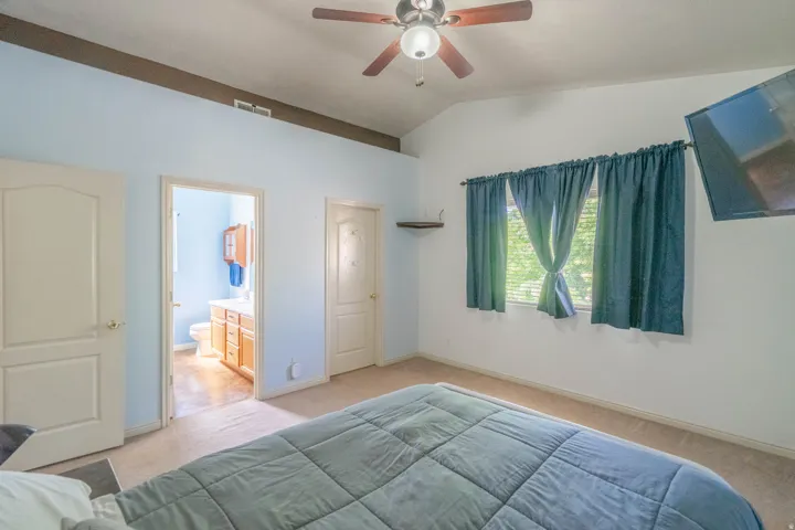 Vaulted ceiling room with ceiling fan, two windows, and carpet flooring