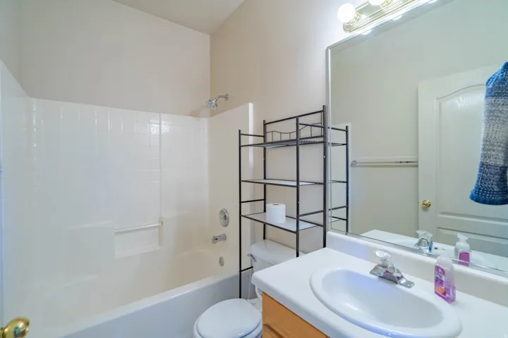 Bathroom featuring a white bathtub with subway tile surround, white vanity countertop with integrated sink, wood-finish vanity cabinetry, and a large wall-mounted mirror with overhead lighting
