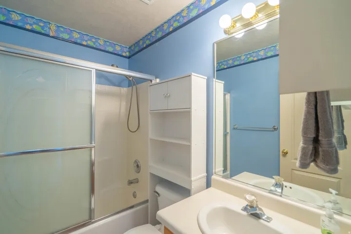 Bathroom featuring a built-in shower/tub combination with sliding frosted glass doors, white vanity with an integrated sink, wall-mounted mirror, and a wall-mounted vanity light fixture
