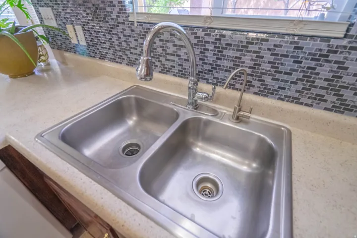 Stainless steel double basin sink with a gooseneck faucet and separate filtered water dispenser