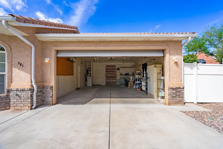 Attached two-car garage with a concrete driveway, stucco exterior, brick wainscoting, and white rain gutters