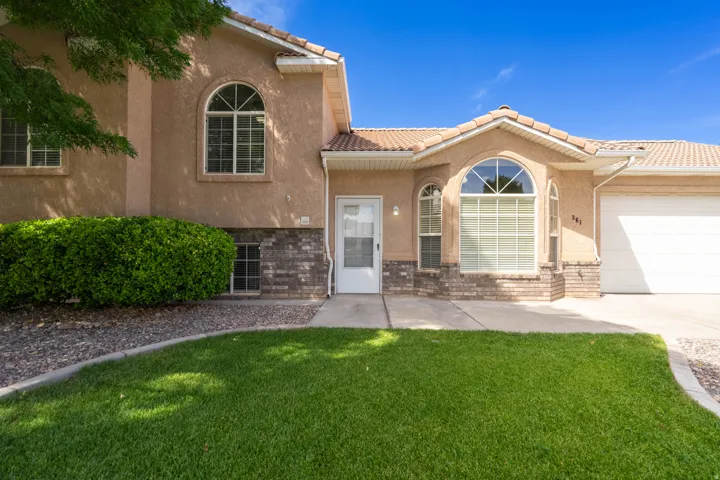 Stucco exterior featuring arched windows, brick detailing, a tiled roof, a concrete driveway, and a manicured lawn