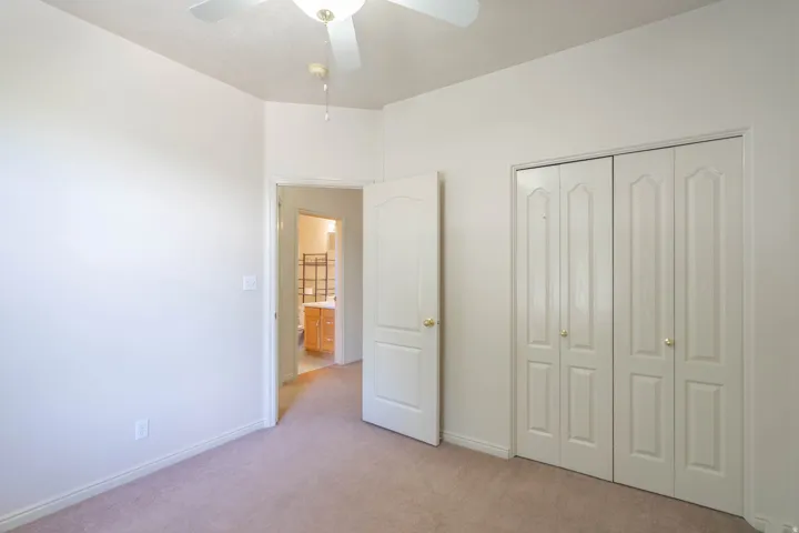 Neutral-toned carpet flooring and light-colored walls define this room, featuring a ceiling fan with integrated lighting