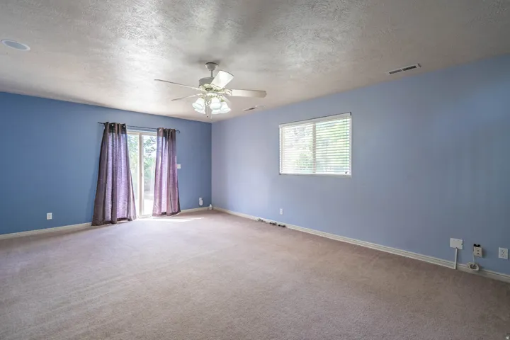 Expansive carpeted room featuring a ceiling fan with integrated lighting, recessed lighting, and a sliding glass door with drapes