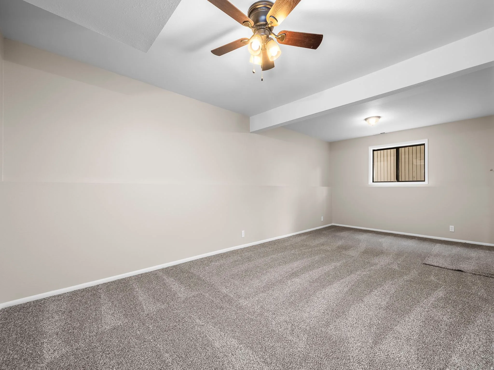Spacious room featuring neutral wall paint, gray carpeting, a ceiling fan with integrated lighting, a recessed light fixture, and a window with blinds