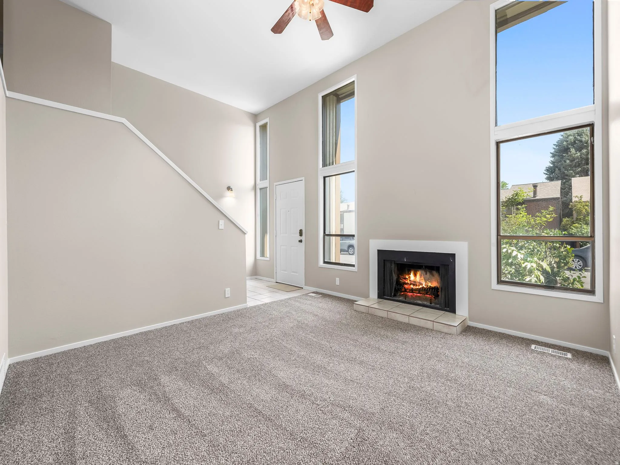 Living area featuring a fireplace with a tiled hearth, high ceilings, large windows, and gray carpeting