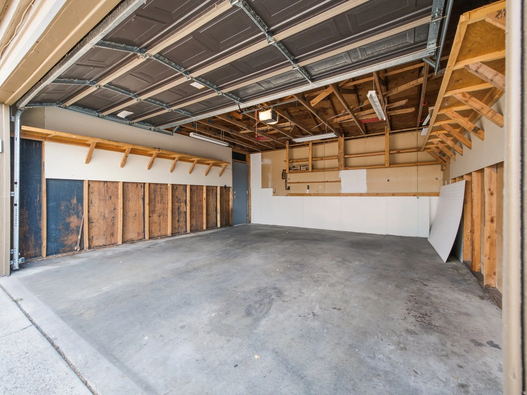 Spacious garage featuring a concrete floor, exposed wooden ceiling joists, overhead fluorescent lighting, and built-in shelving