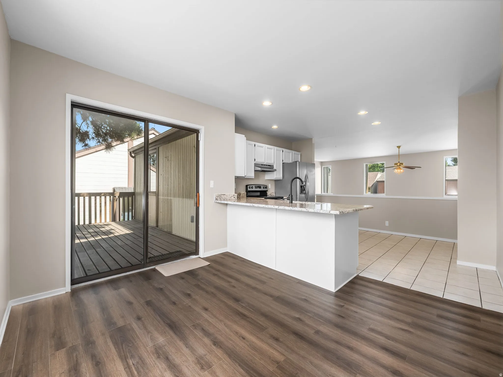 Open-concept living area with wood-finish flooring, a kitchen island with stone countertop, white cabinetry, and recessed lighting