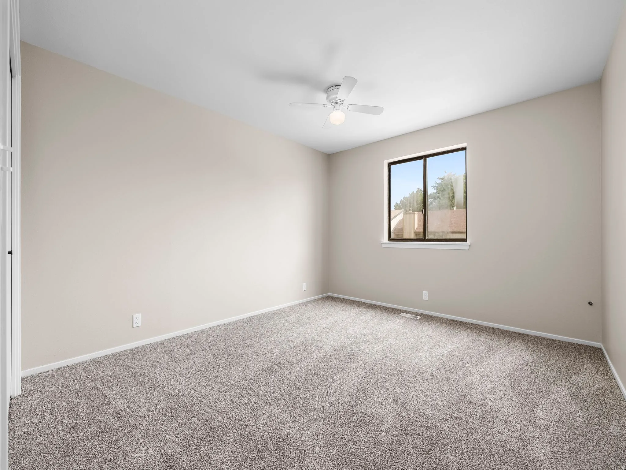 Spacious room featuring neutral carpeting, light-toned walls, a single window, and a ceiling fan with integrated lighting