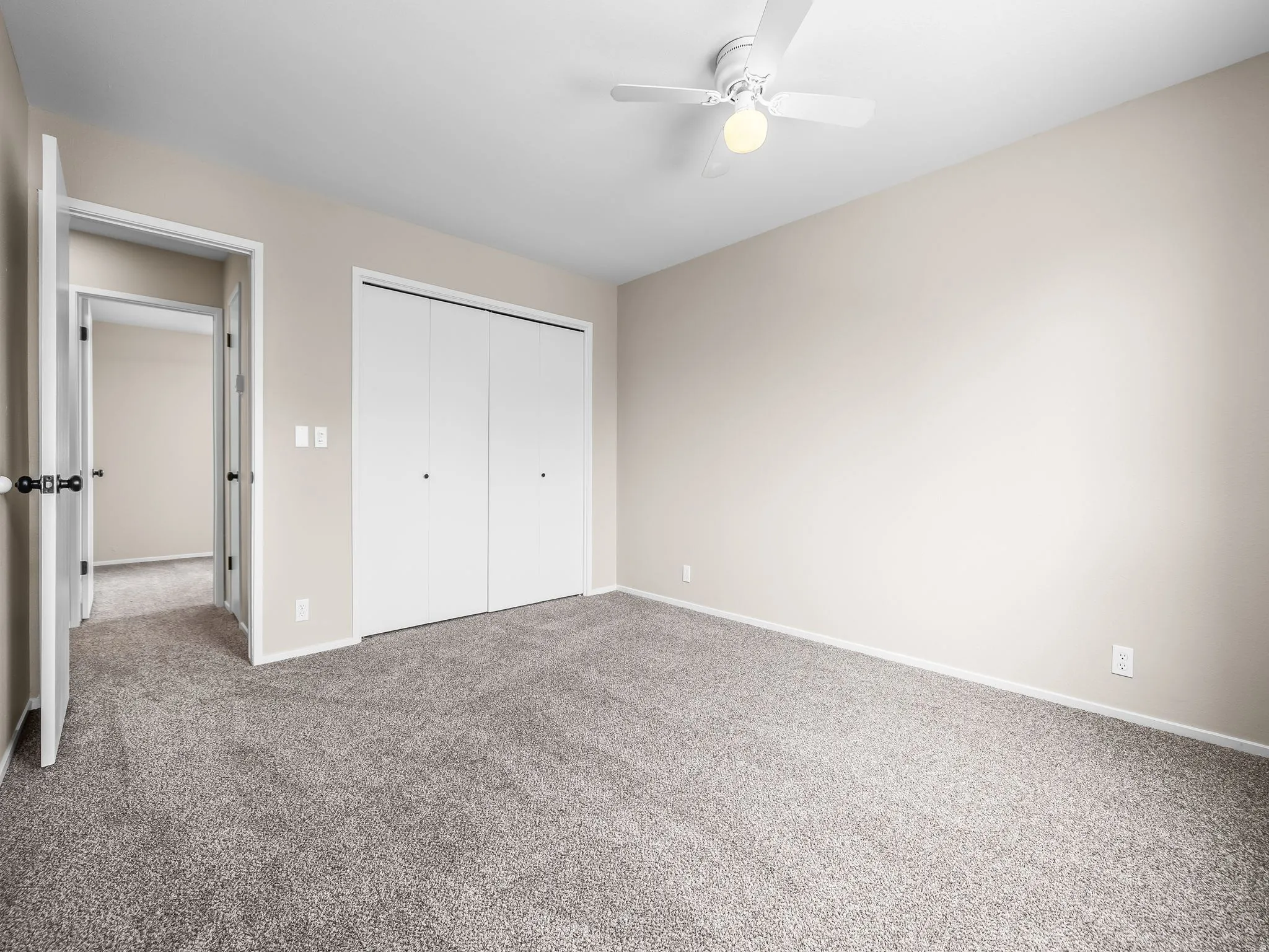 Neutral wall color, grey textured carpet, white bi-fold closet doors, white ceiling fan with integrated lighting, and white trim