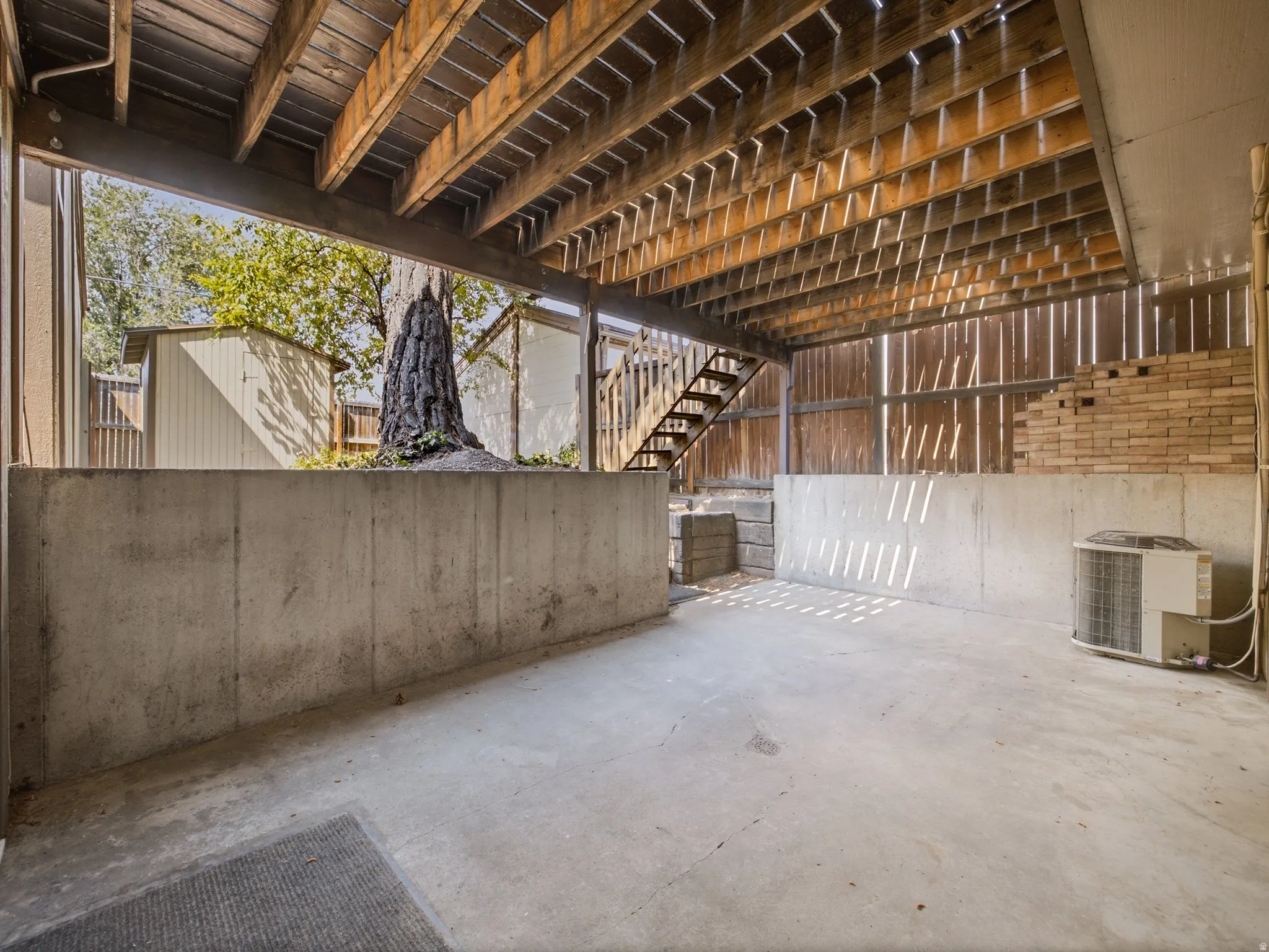 Concrete patio featuring a wood-framed deck overhead and a partial brick wall