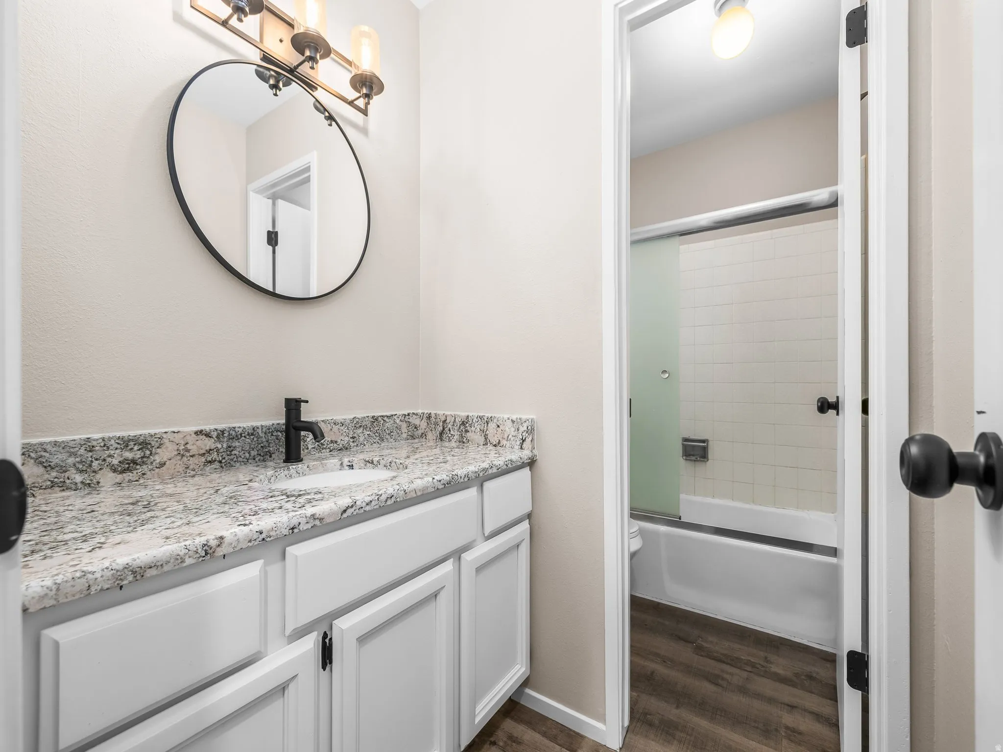 Bathroom featuring a vanity with a light-toned stone-finish countertop, white cabinetry, and a circular mirror