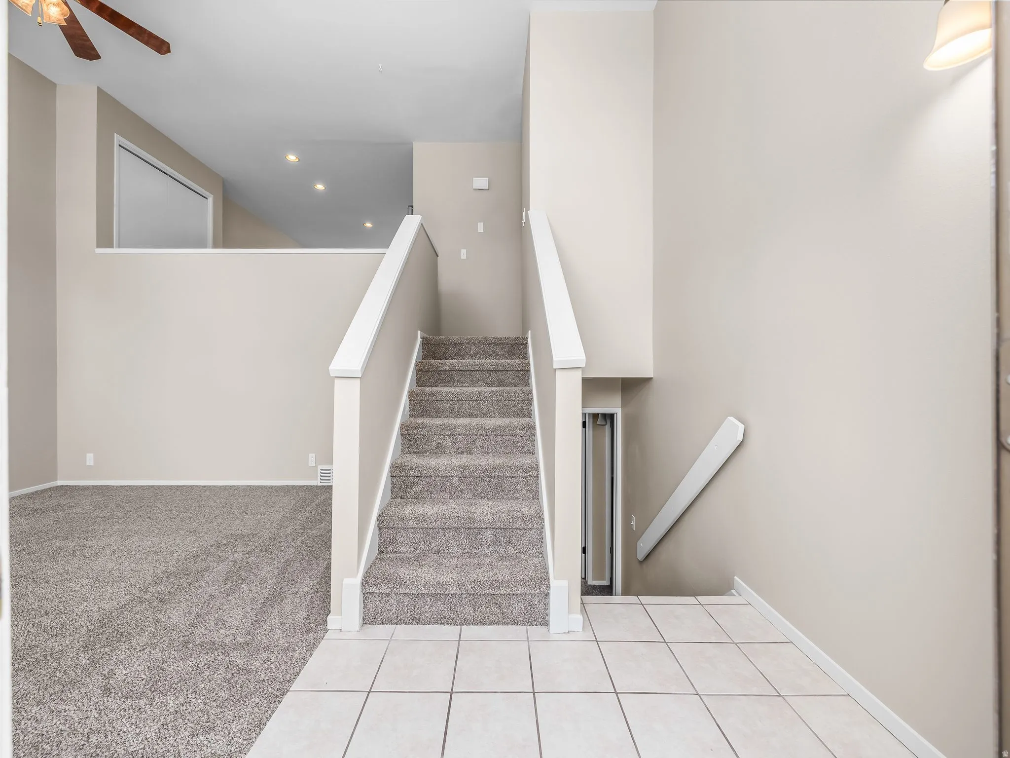 Entryway featuring a tiled floor, carpeted stairs with white railings, and a carpeted living area