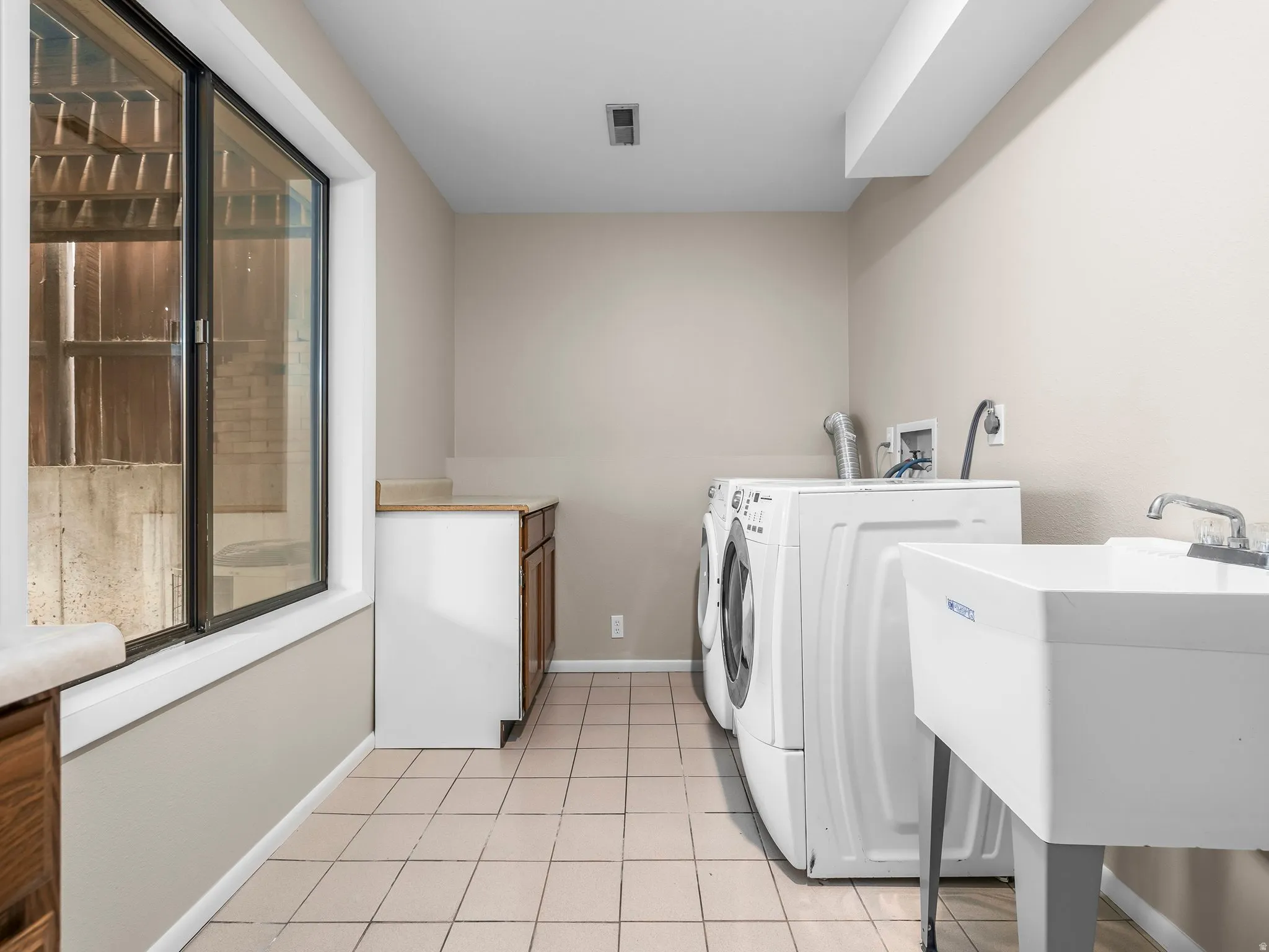 Utility room featuring tile flooring, a large window, built-in cabinetry with a countertop, and a utility sink