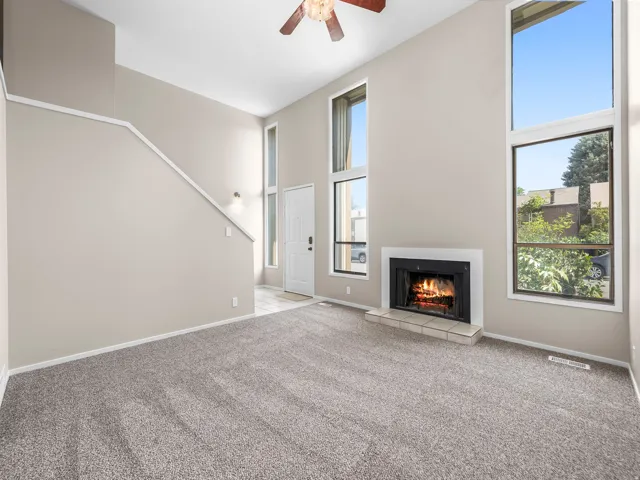 Living area featuring a fireplace with a tiled hearth, high ceilings, large windows, and gray carpeting