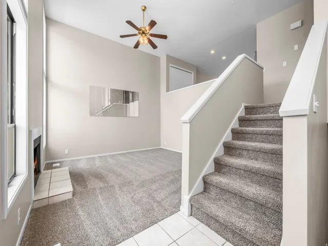 Living area featuring a vaulted ceiling with a ceiling fan, a fireplace with a tiled hearth, and carpet flooring