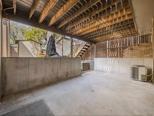 Concrete patio featuring a wood-framed deck overhead and a partial brick wall