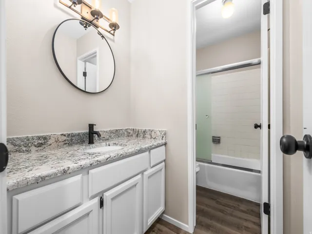 Bathroom featuring a vanity with a light-toned stone-finish countertop, white cabinetry, and a circular mirror
