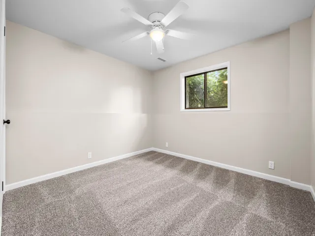 Carpeted room featuring a ceiling fan with integrated lighting, a window with white trim, and light-toned walls