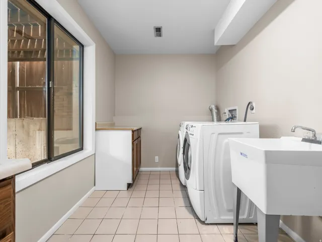Utility room featuring tile flooring, a large window, built-in cabinetry with a countertop, and a utility sink