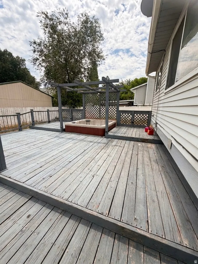 Spacious outdoor deck featuring a built-in hot tub with a pergola, perimeter railing, and exterior siding