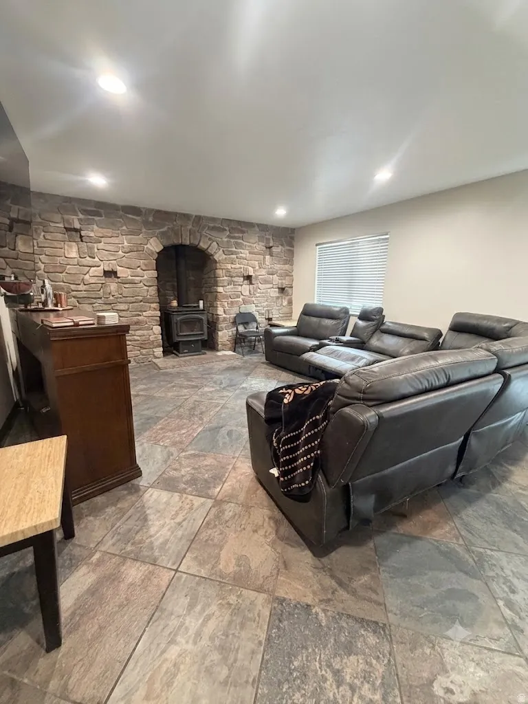 Spacious interior featuring a stone accent wall, recessed lighting, and a prominent wood-burning stove within an arched stone alcove