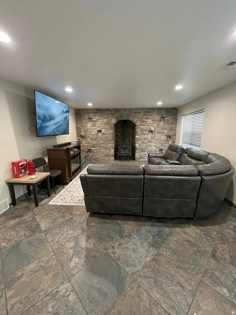 Living area featuring a stone accent wall with an arched opening, a wood-burning stove, recessed lighting, and large format tile flooring