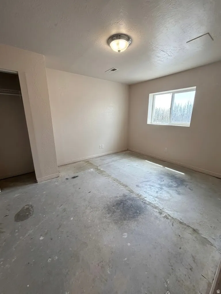Spacious room featuring neutral painted walls, a window, and an overhead light fixture