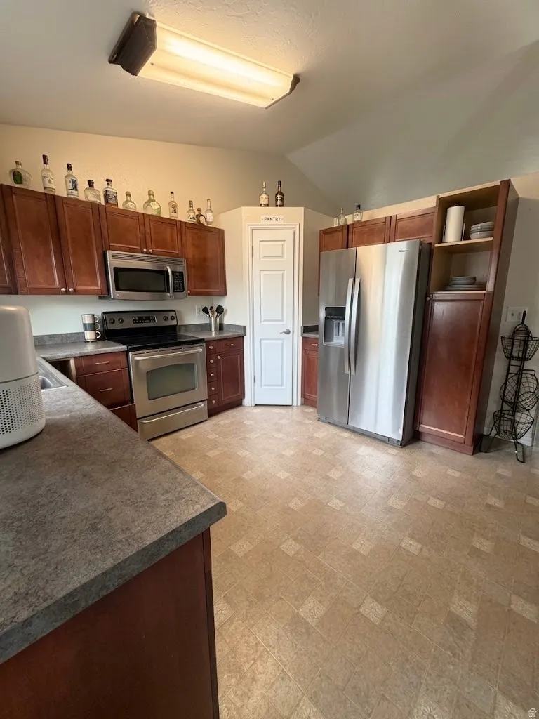 Kitchen featuring wood-finish cabinetry, stainless steel appliances, and a pantry door