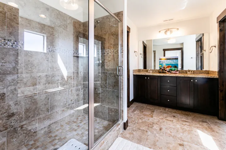 Spacious bathroom featuring a glass-enclosed shower with stone tile surround, mosaic accent band, and integrated shelving