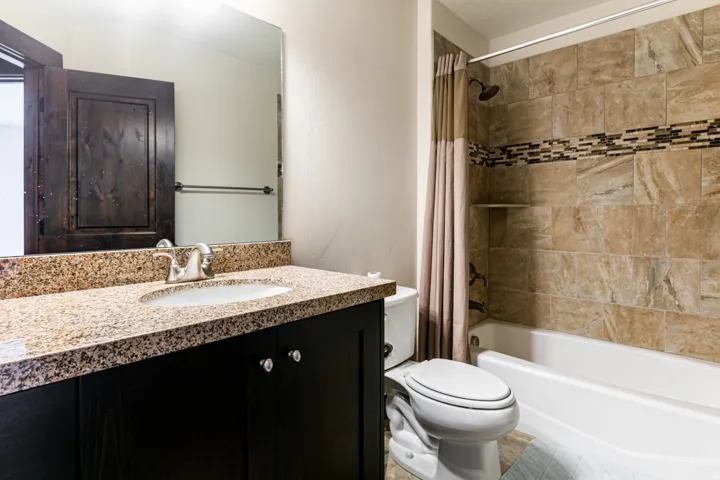 Bathroom featuring a single vanity with a granite countertop, undermount sink, and dark wood-finish cabinetry
