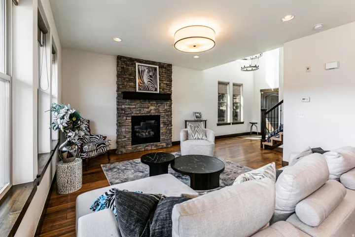 Spacious living area featuring a stone-clad fireplace with a dark wood mantel, recessed lighting, and rich wood-finish flooring