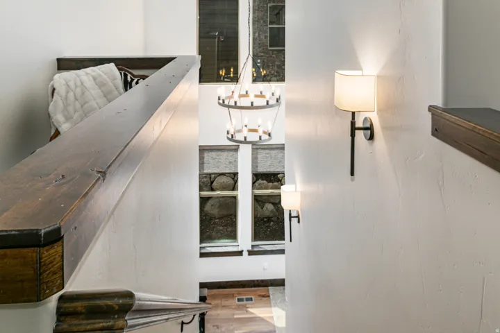 Stairwell featuring a rich wood handrail, white textured walls, and modern sconce lighting
