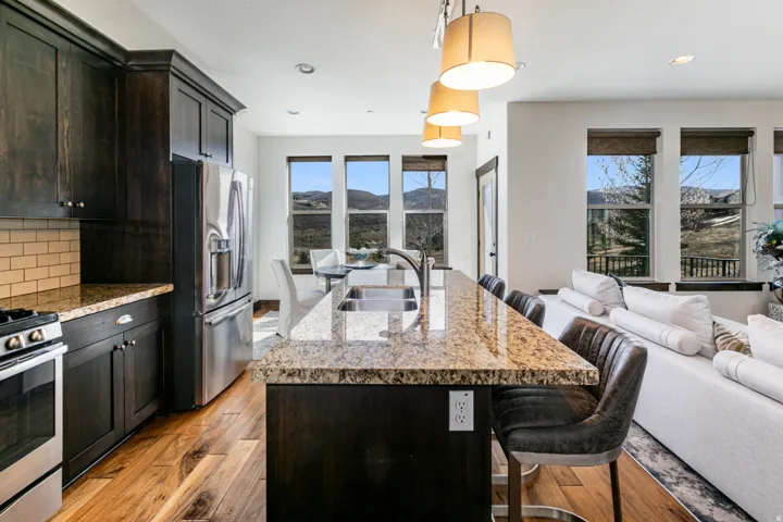 Spacious kitchen featuring dark wood cabinetry, stainless steel appliances, and a light-toned granite countertop with an undermount sink