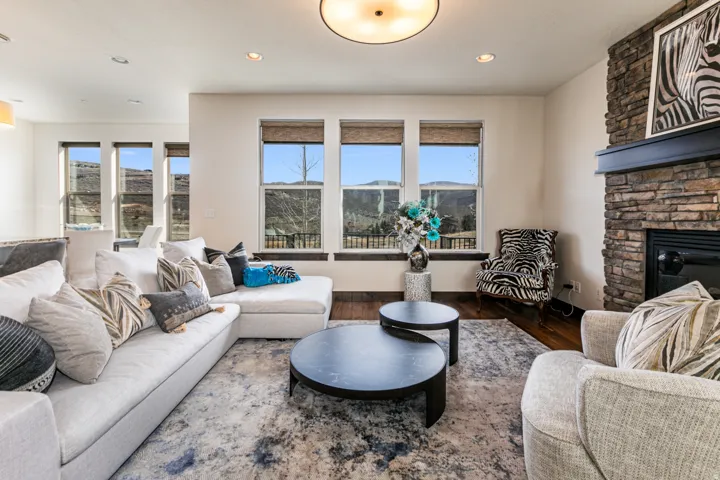 Spacious room featuring multiple large windows, a stone-clad fireplace with a dark mantel, wood-finish flooring, and recessed lighting