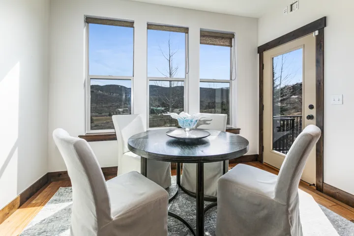 Bright dining area featuring three large windows, a glass-paned door, wood-finish flooring, and dark wood trim
