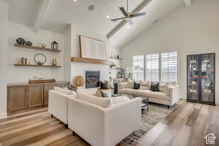 Vaulted ceiling with exposed beams, wood-finish flooring, built-in cabinetry, fireplace with wood mantel, and plantation shutters